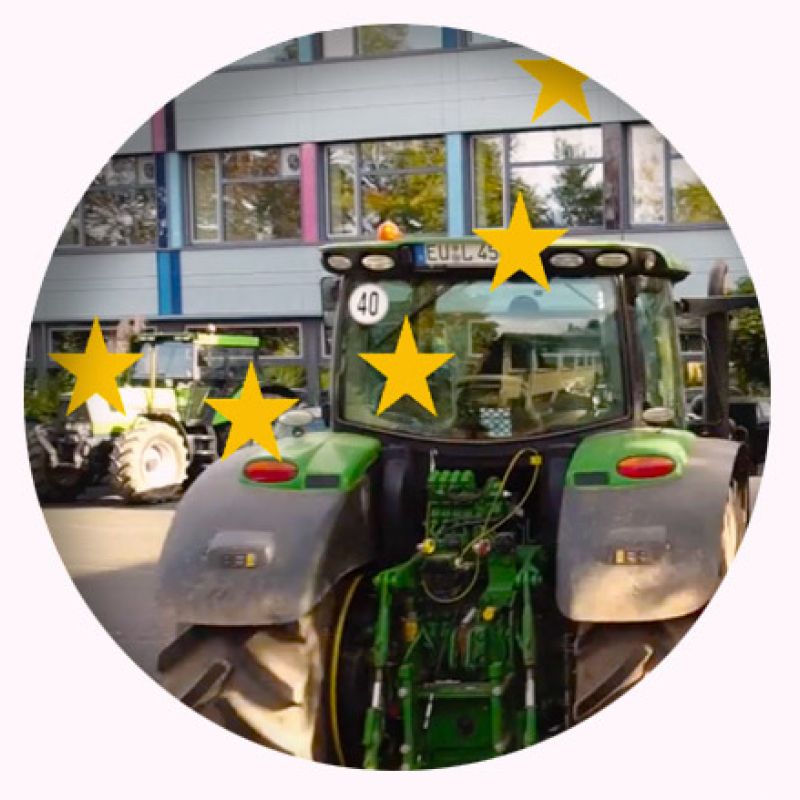 Ein Traktor fährt auf einen Schulhof Parkplatz, darüber liegen gelbe Europa Sterne